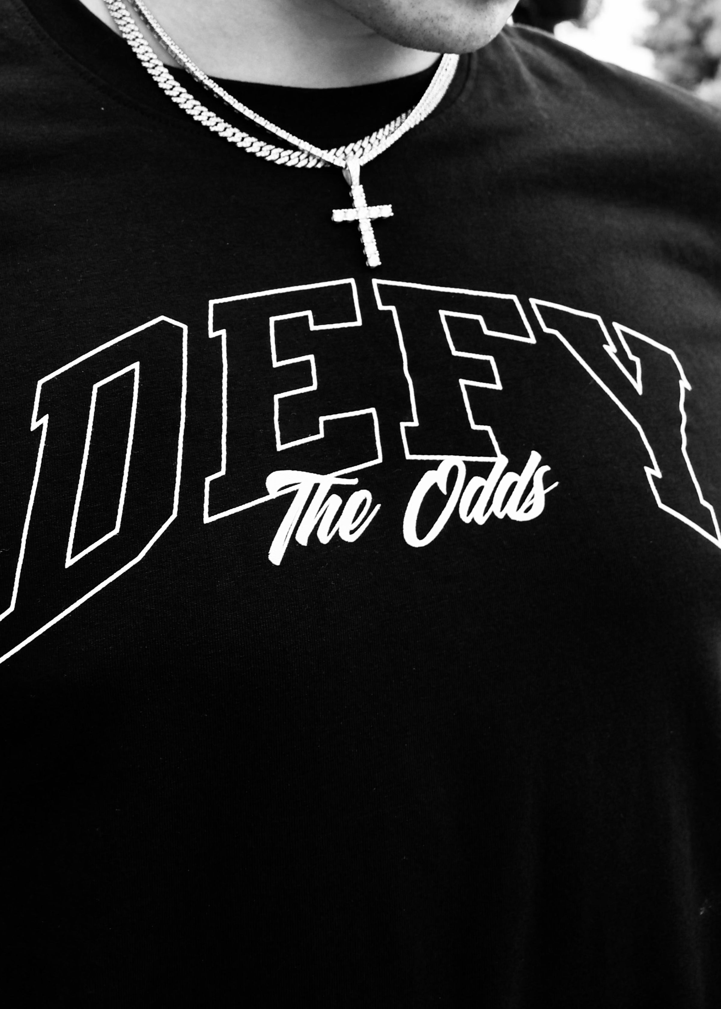 Black t-shirt with 'DEFY The Odds' text and a necklace worn by a person.